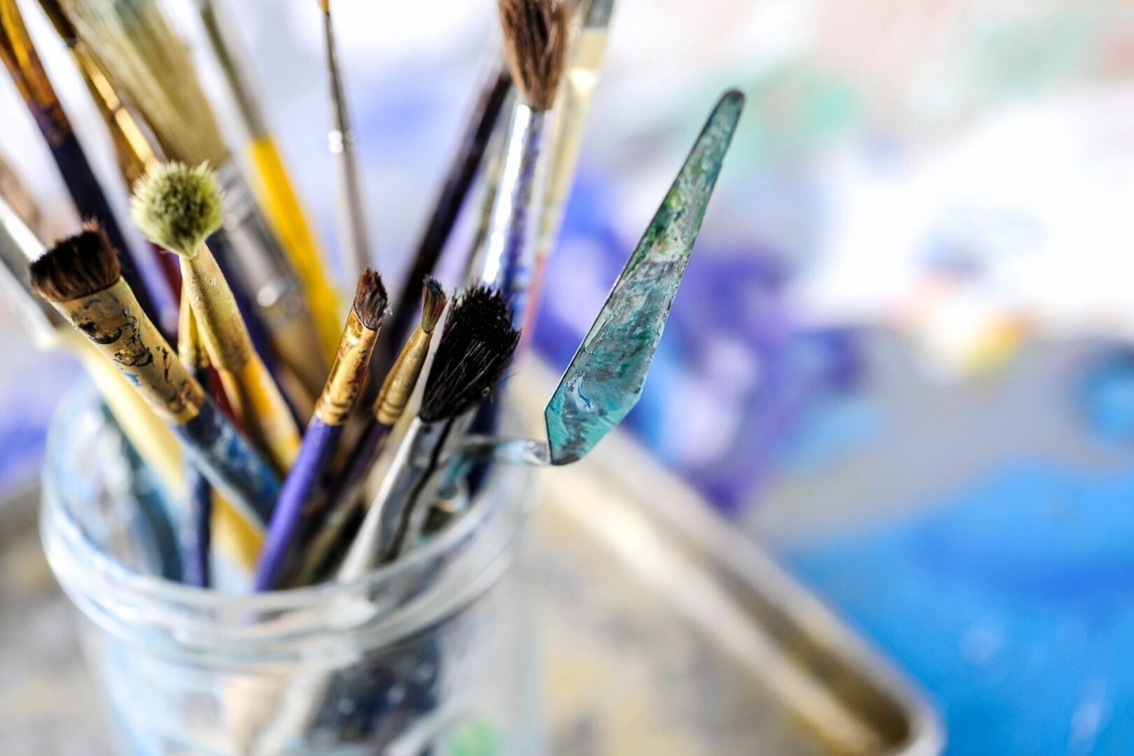 A glass filled with paint brushes and a blue stick.